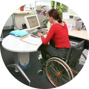Woman with a disability is in her wheelchair at her desk working on a computer.
