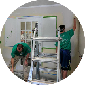 A candid shot of two men in green Comcast Cares t-shirts work in the North Augusta office painting walls.