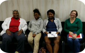The I'm Sweet Peer Support group with four consumers sitting in a row looking at the camera smiling. The women are a variety of ages from young adult to older consumers.