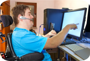 Man in a wheelchair with Cerebral Palsy works at an adapted desk using assistive technology to lead an independent life as a person with a disability.