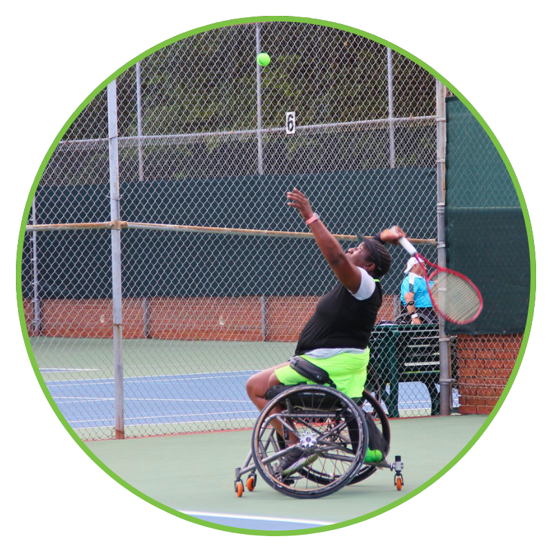 Image is circle shaped with a green border. Background is a green tennis court. In the foreground is a black female wheelchair tennis player preparing to serve.