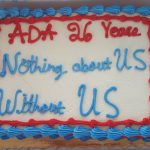 An anniversary cake with blue and red trim with text: ADA 26 Years, Nothing about US without US