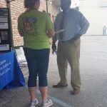 A staff member chats with one of the guests. Photo: A female staff member wears a green ADA25 celebration shirt with her back to the camera, speaking with a gentleman in a blue shirt and tie.