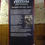 A roll-up banner with information about the Road to the ADA. There is text along with black and white images during the disability rights movement leading up to the signing of the ADA.