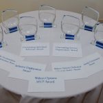 The seven clear, acrylic awards with blue bases sit arranged with envelopes containing the winners' information sit on a table prior to the ceremony.