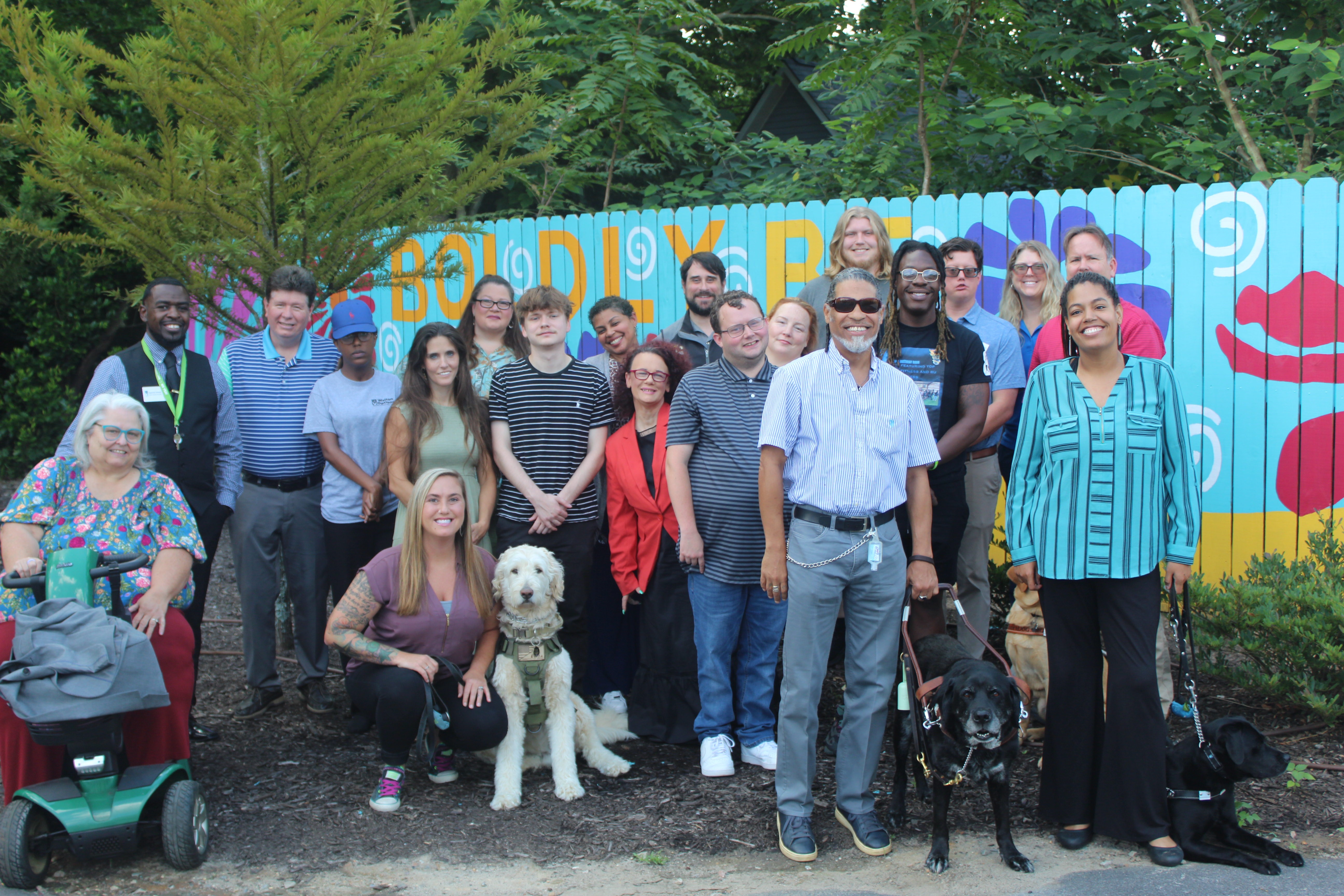 A large group of diverse people and service dogs standing outside and posing for a photo.