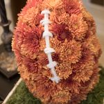 To celebrate the theme of the evening, a flower centerpiece that has brown flowers arranged in the shape of a football nestled in a bed of greenery that looks like turf.