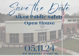 The background of photo is a building with text that reads: Save the date Aiken public safety open House 05-11-24 834 Beaufort street NE