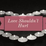 A series of tea light candles are arranged in the shape of a heart and are lit. over the center of them is a pink text banner with the text: Love Shouldn't Hurt